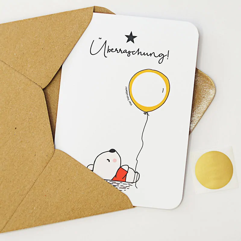 Rubbelkarte mit einem Bär, der einen Luftballon (mit beschreibbarem Rubbelfeld) hält und der Überschrift "Überraschung"